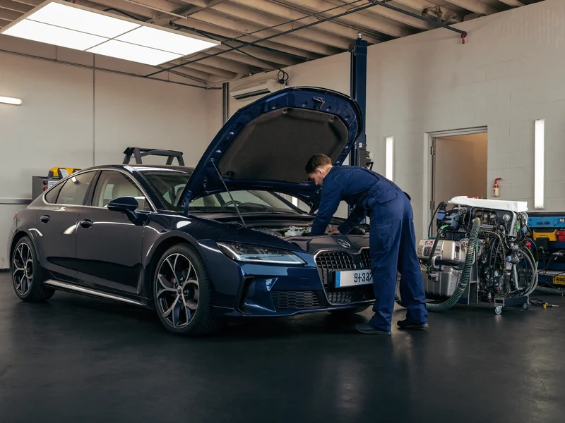 Osobní auto s otevřenou kapotou v čisté dílně a servisní stanice klimatizace vedle něj